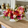 Mixed bouquet of pink, orange, and peach flowers in a white bowl vase