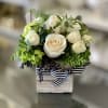 White roses and green flowers arranged in a small wooden box with a striped ribbon
