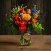 Mixed bouquet of red, orange, yellow, and blue flowers in a glass jar