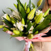Hand-tied bouquet of white lilies and green buds wrapped in pink paper with ribbons