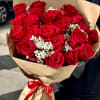 Large bouquet of red roses with white filler flowers wrapped in brown paper and a red ribbon