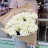 Large bouquet of white roses wrapped in kraft paper, held by a person outside a shop
