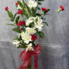 White alstroemeria and red carnations in a clear glass vase with a red bow.