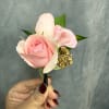 Pink rose boutonniere with pale petals and gold filler held in hand