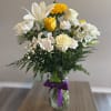 Bouquet of white and yellow flowers in a glass vase with a purple ribbon