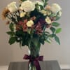 Bouquet of white roses and mixed flowers in a glass vase with a purple ribbon