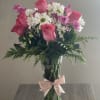 Pink roses and white daisies in a clear glass vase with a pink ribbon