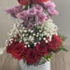 Red roses and purple flowers arranged in a glass vase