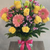 Bouquet of yellow roses and pink gerbera daisies in a glass vase with a pink ribbon