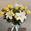 Yellow roses and white lilies arranged in a glass vase with a white ribbon.