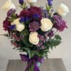 Bouquet of white roses, purple blooms, and a purple ribbon in a glass vase