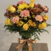 Yellow roses and pink carnations in a glass vase with a gold ribbon