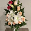 Bouquet of peach roses, white lilies, and red carnations in a glass vase