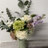 Mixed bouquet of roses, hydrangea, and lavender flowers in a pale green vase