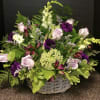 Basket arrangement of lavender roses, purple blooms, and white flowers