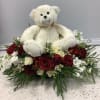 White teddy bear sitting in a red and white rose arrangement
