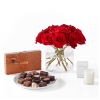 Red roses in a glass vase with chocolates and a candle