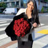 Woman holding a large bouquet of red roses wrapped in black paper