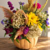 Mixed bouquet in a pumpkin-shaped container with yellow and purple flowers