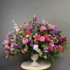 Large mixed bouquet of pink, purple, and red flowers in a white urn vase