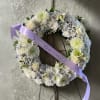 White floral wreath on a stand with a lavender ribbon