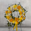 Yellow and white floral wreath on a black stand with a ribbon
