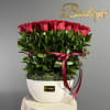 Red roses arranged in a white vase with a burgundy ribbon