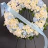 Standing wreath of white and pale blue flowers with a light blue message ribbon on an easel.