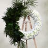 Large floral wreath with white flowers and dark palm fronds on an easel