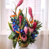 Tropical arrangement with pink ginger, bird of paradise, and orchids in a gold vase