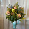 Bouquet of peach roses and yellow filler flowers in a turquoise mug vase