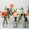 Three small floral arrangements in glass bottles with peach and white blooms