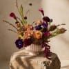 Mixed floral arrangement in a pale pink vase on a stone pedestal