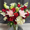 Bouquet of red roses, pink lilies, and white hydrangeas in a glass vase