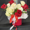 Red and white roses arranged in a pink hat box with a ribbon