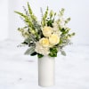 White roses and white flowers arranged in a tall white vase