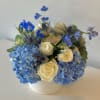 Blue hydrangeas and cream roses arranged in a white vase