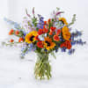 Mixed bouquet of sunflowers, orange roses, and blue flowers in a glass vase