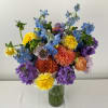 Mixed bouquet of blue, purple, yellow, and peach flowers in a glass vase