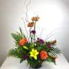 Tropical flower arrangement with orchids, lilies, and orange roses in a black vase