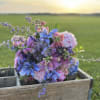 Mixed bouquet of blue, pink, and purple flowers in a wooden crate