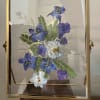 Framed pressed blue and purple flowers with fern leaves in a gold frame