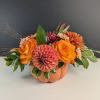 Orange and pink floral arrangement in a pumpkin-shaped container