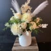 White floral arrangement in a textured white vase with feathery accents