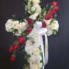Cross-shaped floral arrangement with white flowers and red roses on a dark background