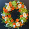 Circular floral wreath with orange and white roses and green orchids on a stand