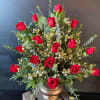 Red roses arranged in a gold vase with mixed greenery