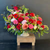 Large mixed bouquet of red, pink, and peach flowers in a white vase