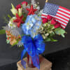 Red, white, and blue floral arrangement with an American flag and blue ribbon