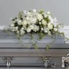 White floral casket spray with trailing ivy on a gray casket